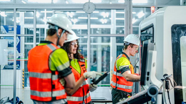 Three engineers program an industrial robot or CNC machine using an AI interface. The team manufactures advanced microchips or high-tech components in a smart factory.