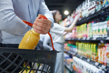 A man is carefully pouring fresh orange juice into a shopping basket
