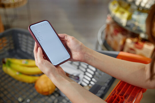 A person is holding a mobile cell phone in front of a shopping cart
