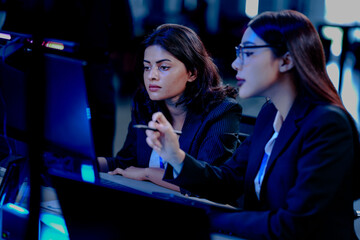 Late night code warriors: Two female developers intensely debugging code together, eyes locked on the screen, determined to solve a complex issue before the product launch.