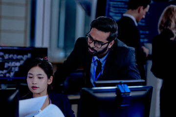 Intense collaboration hub Diverse AI team deep dive into project data late night. Manager guides Asian colleagues reviewing analytics for a new service launch in tech office.