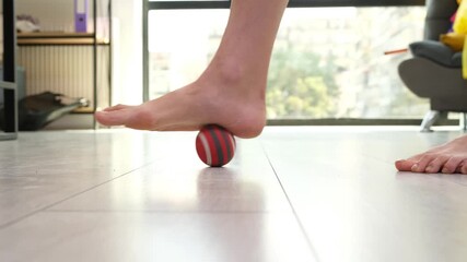 Male bare foot presses small massage ball on smooth floor for simple therapy. Athlete rolls sole back and forth releasing tight plantar muscles