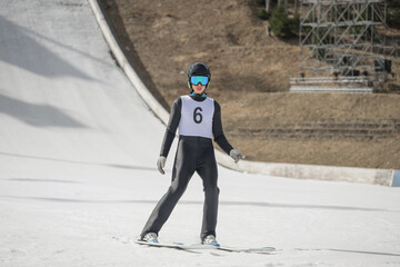 A young ski jumper lands from the ramp during a training session on a sunny winter day.