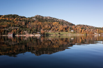A serene autumn seaside scene shows colorful trees on hillsides, Norway