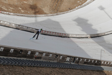 A ski jumper soars through the air off a snowy ramp, showcasing skill and focus during winter sports competition.