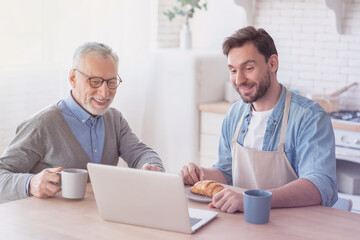 Happy loving senior old elderly father having breakfast in the kitchen with his adult son, preparing food and meal, cooking lunch and dinner together. Happy father`s day! I love you, dad!