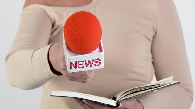 Woman journalist reads from a notebook while holding a NEWS microphone