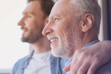 Close up shot of a caucasian young adult son supporting his old elderly senior man looking at the window in future together at home. Happy father`s day! I love you, dad!