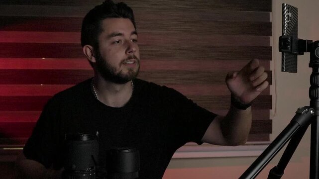Male vloggeri nstructor sitting in a dark studio, talking directly to the camera