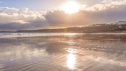 A sandy beach with heavy clouds above and headlands are in the distance.