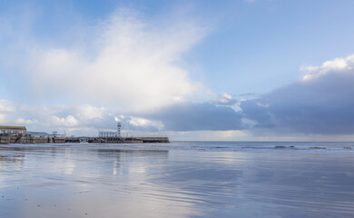 A beach and lighthouse where a receding tide has left ripples of water on the sand.