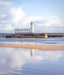 A beach and lighthouse where a receding tide has left ripples of water on the sand.