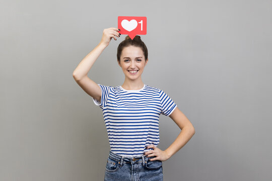 Woman holding heart like icon of social media over her head, looking at camera with toothy smile.
