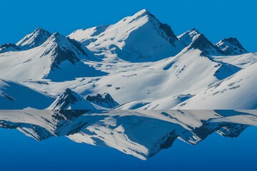 Fototapeta premium Snow covered mountain range with reflection in clear blue water under bright sky winter peak
