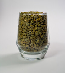 A glass filled with unroasted green coffee beans.