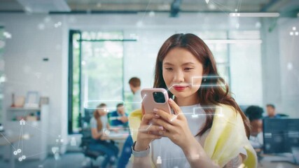 Asian female holding smartphone and scrolling message feed in bright workplace. Standing near group of coworkers while digital interface elements floating around in modern office environment. - Powered by Adobe