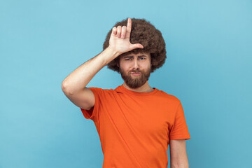 Man holding hand near forehead showing loser gesture with fingers, having problems, looks unhappy.