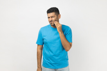 Sick unshaven man frowning his face, touching painful cheek, suffering terrible toothache.