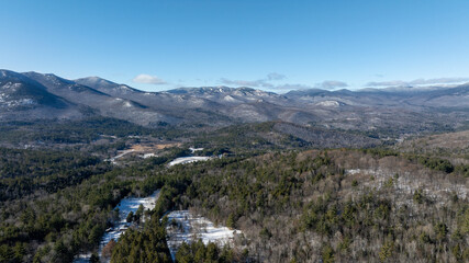 Panoramic winter view of the Adirondack Mountains in New York with forested valleys, snow patches, and clear blue sky.