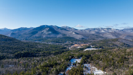 Panoramic winter view of the Adirondack Mountains in New York with forested valleys, snow patches, and clear blue sky.