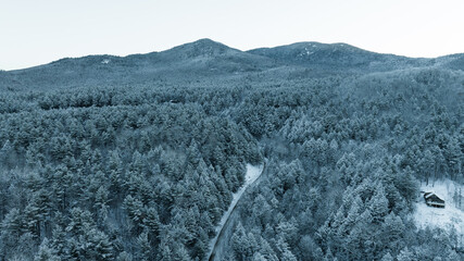 Aerial winter view of snow-covered Adirondack forest, winding road, and mountain peaks in upstate New York.