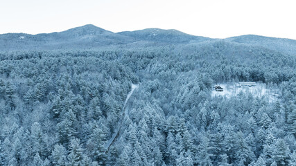 Aerial winter view of snow-covered Adirondack forest, winding road, and mountain peaks in upstate New York.