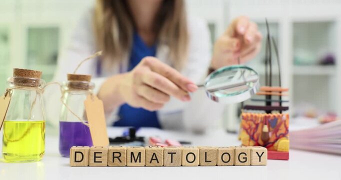 Wooden blocks spell word Dermatology on bright medical table. Woman doctor holds magnifying glass over skin samples while writing notes slow motion