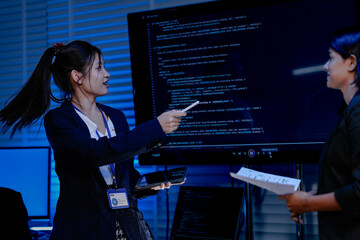 A diverse team with an Asian female, an Indian female and a Caucasian male collaborates in a high-tech office. They are standing and discussing a project.