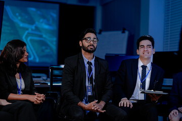 A large IT department meeting in a command center (SOC). A senior developer explains an AI algorithm and cybersecurity protocol to the entire engineering team.
