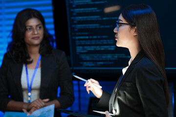 A female tech leader, an Asian woman, presents a new digital transformation strategy using a tablet. Her diverse team discusses sustainable AI solutions for future growth.