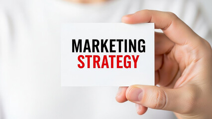 Person holding a card with marketing strategy written in black and red bold letters on a white card