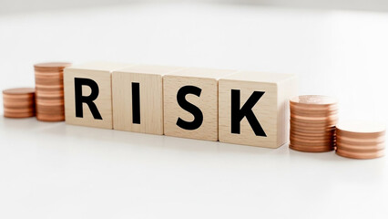 Risk spelled out in wooden blocks with stacks of coins on a white surface representing investment