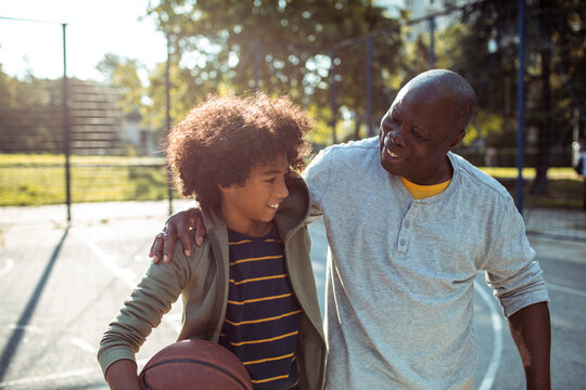 Senior grandfather and child grandson smiling after basketball at outdoor court
