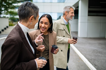 Adult and mature coworkers smiling during coffee break outside office