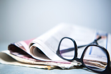 A pile of newspapers and glasses on the table.