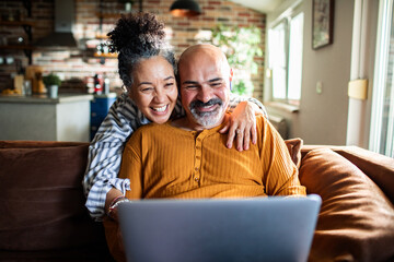 Mature couple laughing while using laptop on sofa at home