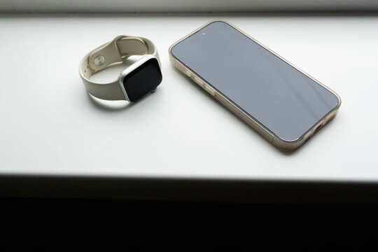 Modern smartwatch and smartphone resting on a window sill in a cozy indoor setting during daylight hours
