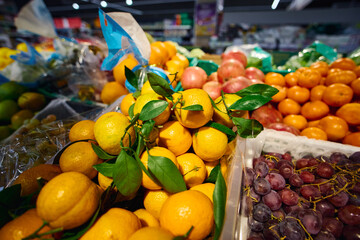 Vibrant display of fresh citrus fruits and grapes in a grocery store during daylight hours