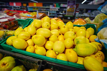 Lemons are piled high in a green basket at a grocery store