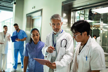 Mature doctor guiding young medical team in hospital hallway focused