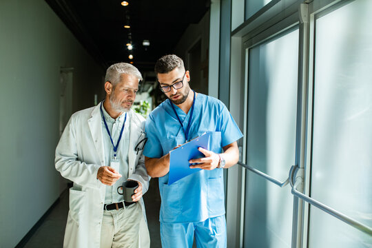 Mature male doctor and young nurse reviewing notes in hospital corridor, focused