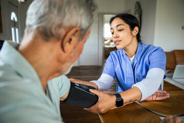 Young nurse checking senior man's blood pressure at home with focused care