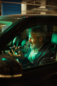 Mature man smiling, using voice assistant in car at night