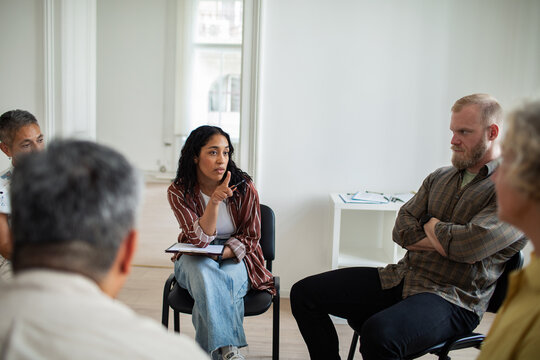 Young adult woman leading support group in bright room, serious