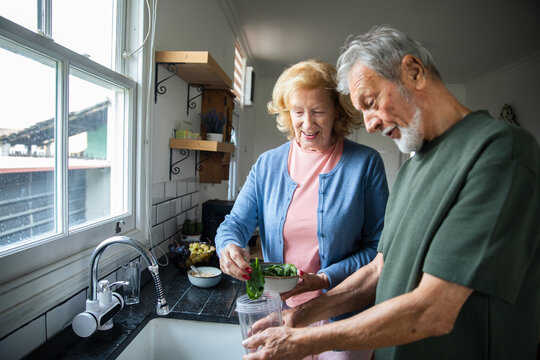 Senior couple smiling while making a healthy smoothie in home kitchen