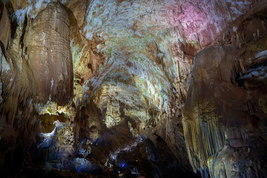 Enormous illuminated cave hall with flowstone columns and textured limestone ceiling