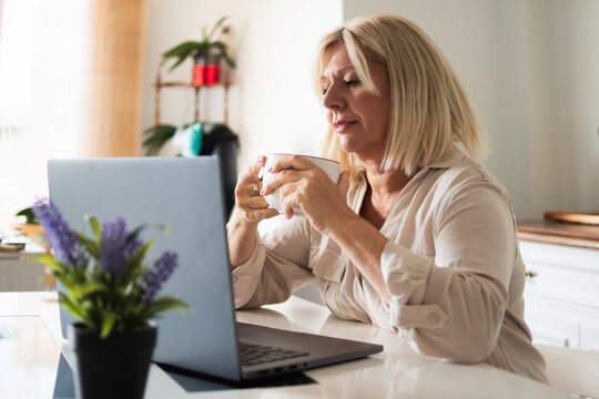Mature woman working remotely from home with laptop and coffee