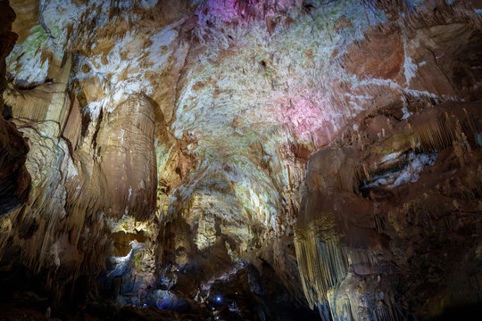 Enormous illuminated cave hall with flowstone columns and textured limestone ceiling