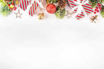 Fototapeta premium White background with Christmas and New Year festive border contains gift boxes, Christmas fir tree branches, decorations and holiday baubles