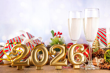 Obraz premium Festive Christmas and New Year 2026 background with champagne glasses, holiday baubles, Christmas tree decor, gift boxes